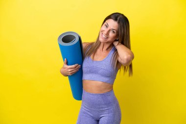 Spor kadını yoga derslerine giderken elinde paspas tutarken sarı olmayan bir arka plan gülüyor.