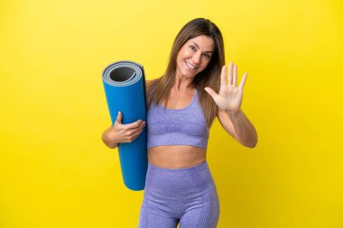 Elinde paspas tutarken yoga derslerine giden sporcu kadın sarı olmayan arkaplan beş parmaklı sayıyor.