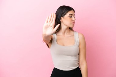 Pembe arka planda izole edilmiş genç bir İtalyan kadın dur hareketi yapıyor ve hayal kırıklığına uğruyor.