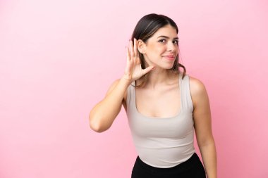 Pembe arka planda izole edilmiş genç bir İtalyan kadın. Kulağına elini sürerek bir şeyler dinliyor.