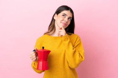 Elinde kahve makinesi olan genç bir İtalyan kadın pembe arka planda izole edilmiş bir şekilde yukarı bakıyor.