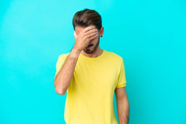 Kafkasyalı genç adam mavi arka planda izole edilmiş, baş ağrısı var.