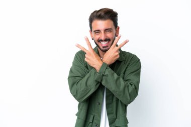 Beyaz arka planda izole edilmiş genç beyaz adam gülümsüyor ve zafer işareti gösteriyor.