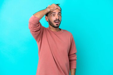 Genç beyaz adam mavi arka planda izole edilmiş. Önüne bakarken sürpriz jest yapıyor.