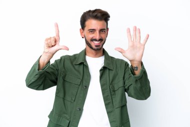 Beyaz arka planda izole edilmiş genç beyaz adam yediyi parmaklarıyla sayıyor