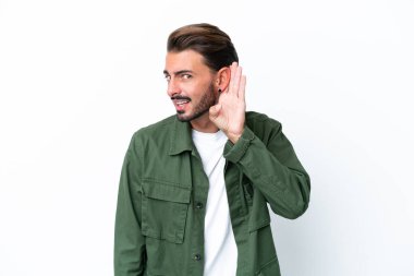 Beyaz arka planda izole edilmiş genç beyaz bir adam. Kulağına elini sürerek bir şeyler dinliyor.