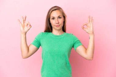 Zen pozisyonunda pembe arka planda izole edilmiş genç bir İngiliz kadın.