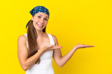 Sarı arka planda izole edilmiş genç bir İngiliz kadın davet edildiği için ellerini yana uzatıyor.