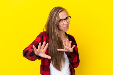 Sarı arka planda izole edilmiş genç bir İngiliz kadın gergin ellerini öne uzatıyor.