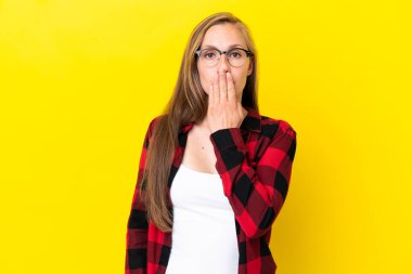 Sarı arka planda izole edilmiş genç bir İngiliz kadın ağzını eliyle kapatıyor.