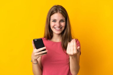 Sarı arka planda izole edilmiş cep telefonu kullanan genç bir kadın, bizimle gelmesi için davet ediyor. Gelmene sevindim.
