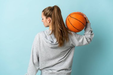 Mavi arka planda izole edilmiş beyaz bir kadın basketbol oynuyor.