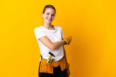Sarı arka planda izole edilmiş genç elektrikçi kadın geriye işaret ediyor