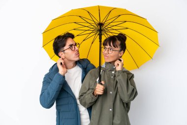 Beyaz arka planda şemsiyesi olan genç ve melez bir çift kafalarını kaşıyarak bir fikir üretiyor.