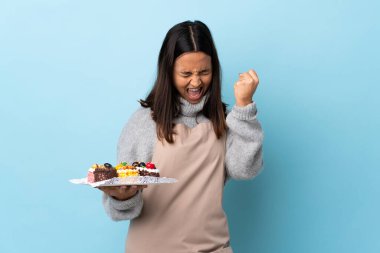 Pasta şefi büyük bir pasta tutuyor ve mavi arka planda zaferi kutluyor..