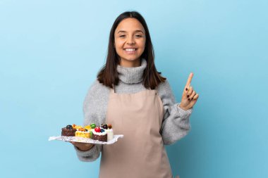 Pasta şefi izole edilmiş mavi arka planda büyük bir pasta tutuyor. Harika bir fikir..