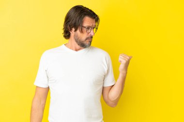 Yaşlı Hollandalı adam sarı arka planda izole edilmiş mutsuz ve kenarı işaret ediyor.