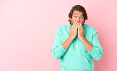 Kıdemli Hollandalı adam pembe arka planda izole edilmiş mutlu ve gülümseyen elleriyle ağzını kapatıyor.