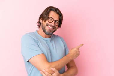 Pembe arka planda izole edilmiş, gözlüklü ve işaret eden yaşlı bir Hollandalı.