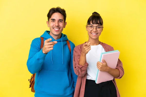 Junges Studentenpaar Auf Gelbem Hintergrund Zeigt Mit Selbstbewusstem Gesichtsausdruck Auf — Stockfoto
