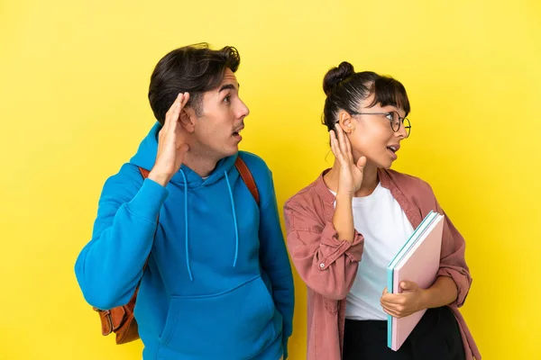 Junges Studentenpaar Isoliert Auf Gelbem Hintergrund Hört Etwas Indem Die — Stockfoto