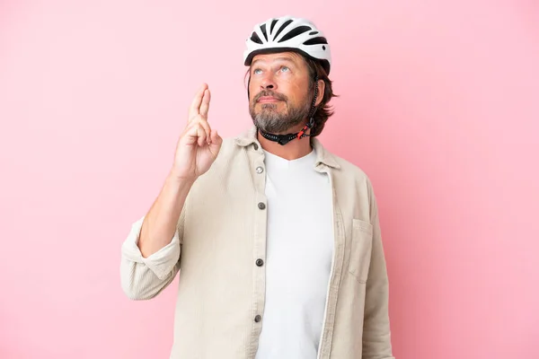 Senior dutch man with bike helmet isolated on pink background with fingers crossing and wishing the best