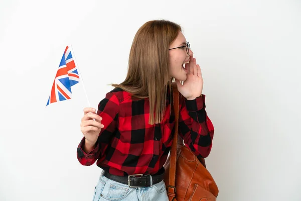 年轻女子举着一面英国国旗 蓝色背景隔离 大张旗鼓地喊着 侧边张大嘴 — 图库照片