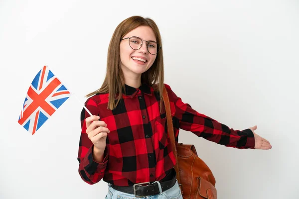 年轻女子举着一面英国国旗 蓝色背景孤立地伸出手 向侧面伸出邀请她来 — 图库照片