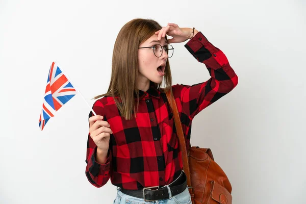 年轻女子举着一面蓝色背景的英国国旗 一边看着侧面 一边惊讶地做着手势 — 图库照片