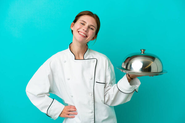 Young chef woman with tray isolated on blue background posing with arms at hip and smiling