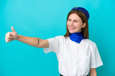 Uçak hostesi İngiliz kadın mavi arka planda izole edilmiş bir şekilde baş parmak hareketi yapıyor.