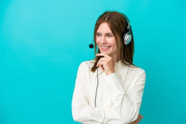 Tele pazarlamacı İngiliz kadın mavi arka planda izole edilmiş bir kulaklıkla çalışıyor.