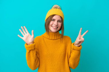 Mavi arka planda, kışlık ceket giyen genç İngiliz kadın parmaklarıyla yediyi sayıyor.