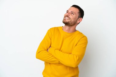 Genç Brezilyalı adam beyaz arka planda izole edilmiş gülümserken yukarı bakıyor