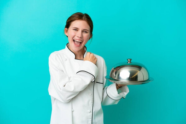 Young chef woman with tray isolated on blue background celebrating a victory
