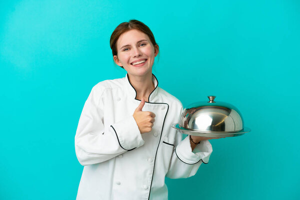 Young chef woman with tray isolated on blue background giving a thumbs up gesture