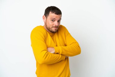 Genç Brezilyalı bir adam beyaz arka planda izole edilmiş. Omuzlarını kaldırırken şüpheyle hareket ediyor.