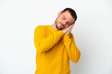Beyaz arka planda izole edilmiş genç Brezilyalı adam uyku jesti yapıyor.