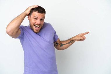 Beyaz arka planda izole edilmiş genç Brezilyalı şaşırmış ve parmağıyla kenarı işaret ediyor.