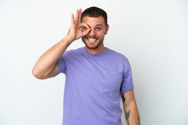 Beyaz arka planda izole edilmiş genç Brezilyalı adam parmaklarıyla tamam işareti gösteriyor