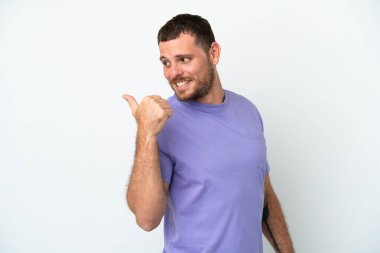 Beyaz arka planda izole edilmiş genç Brezilyalı bir adam bir ürün sunmak için kenarı işaret ediyor