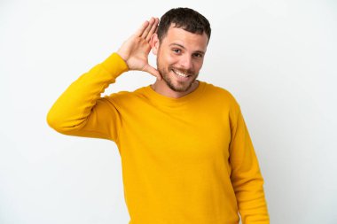Genç Brezilyalı bir adam beyaz arka planda izole edilmiş bir şekilde elini kulağına koyarak bir şeyler dinliyor.