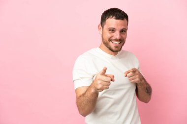 Pembe arka planda izole edilmiş genç Brezilyalı adam şaşırmış ve ön tarafı işaret ediyor.