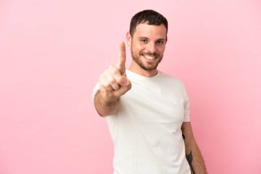 Pembe arka planda izole edilmiş genç Brezilyalı adam parmağını kaldırıyor ve gösteriyor.