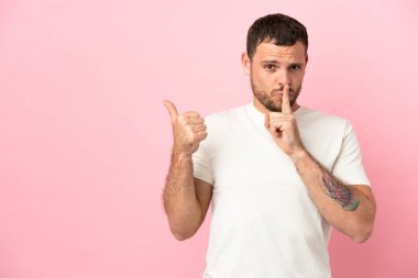Pembe arka planda izole edilmiş genç Brezilyalı adam yan tarafı işaret ediyor ve sessizlik hareketi yapıyor.
