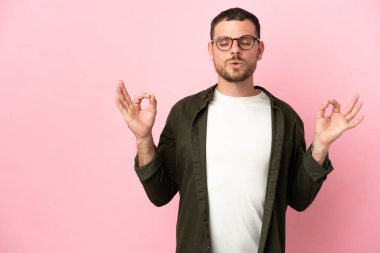 Zen pozisyonunda pembe arka planda izole edilmiş genç Brezilyalı adam.