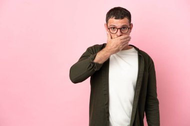 Pembe arka planda izole edilmiş genç Brezilyalı adam ağzını eliyle kapatıyor.