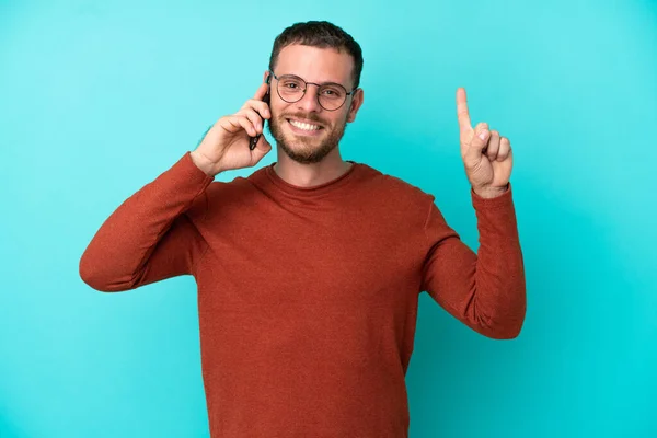 Jeune Brésilien Utilisant Téléphone Portable Isolé Sur Fond Bleu Pointant — Photo