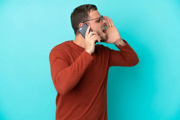 Young Brazilian Man Using Mobile Phone Isolated Blue Background Shouting — Stock Photo, Image