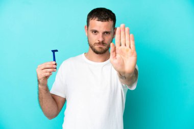 Mavi arka planda sakalını kesen Brezilyalı adam dur hareketi yapıyor.